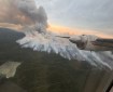 Smoke billows up from a forest fire. Part of an airplane engine is in the photo.