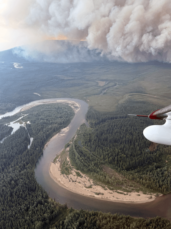 Smoke billows up from a forest fire in the background. Below is a bend in a river.