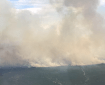 A wall of smoke billows up from a green landscape in this photo taken from an airplane.