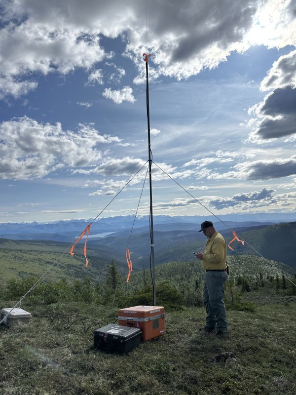 Firefighter installs a repeater station on a ridgetop. Lake and mountains in the background.