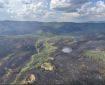 View of fire from the air. Patches of burned forest interspersed with un burned green timber and brush. Isolated smoke plumes in the far left of image.