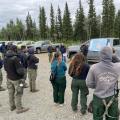 Firefighters gather for a briefing related to the 7 Mile Lookout Fire, with a map displayed on a vehicle in the background.