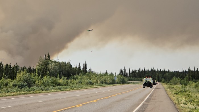 A helicopter with bucket drop approaches a smoke column.