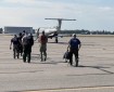 Firefighters walk away from the camera across the tarmac toward a small aircraft with an open door.
