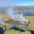 An aerial photo shows wildfire smoke rising into the air from a burned area surrounded by bodies of water.