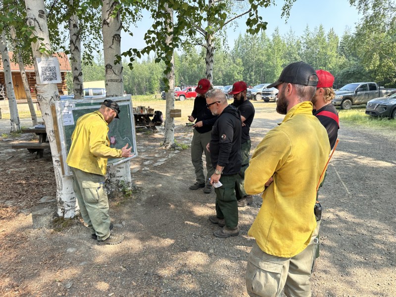 Firefighters in yellow nomex and green pants stand around an operations map discussing