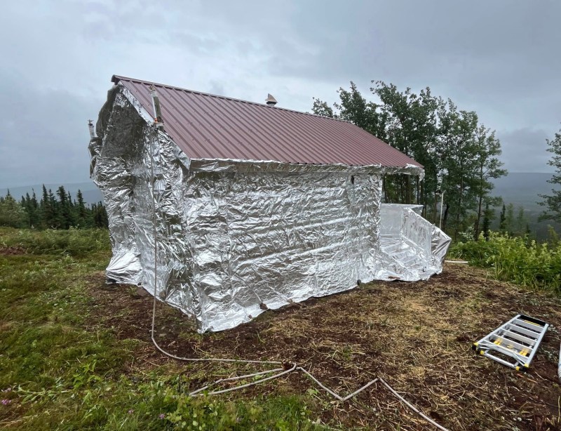Historic Eleazar cabin wrapped in tin-foil like fire resistant material to reduce the risk of fire damage. This is a structure protection tactic.