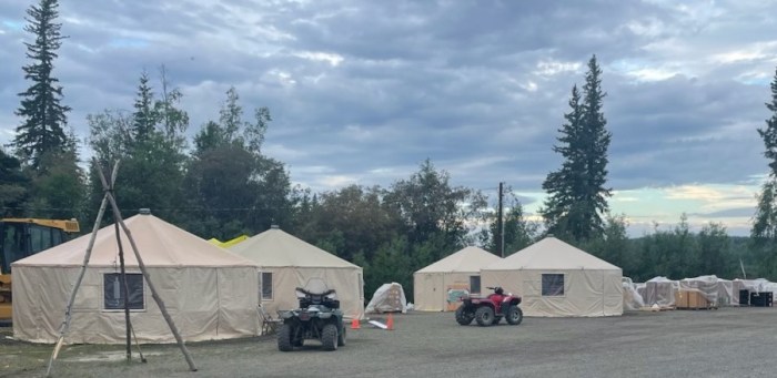 Image shows four tan round yurts that are being used for the incident command post of the Lush Fire. Stacks of supplies are under plastic tarps to the right and two four wheeler vehicles are in fount of the yurts. The sky above is filled with grey clouds.