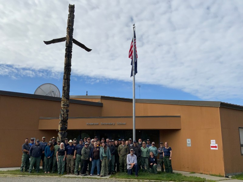 A group of people stands in front of the Anderson School for a group photo.