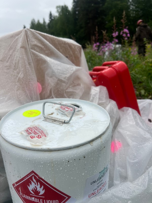 Rain can be seen puddled on top of a fuel container weighing down plastic sheeting covering firefighting supplies.