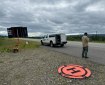 A man with a remote control in hand stands by the side of the road. Behind him is a landing zone for an Unmanned Aerial System.
