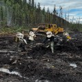 Firefighters working in a muddy area, conducting mop-up operations near heavy machinery in a forested landscape.