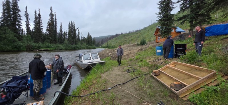 A boat is moored along a river as people work along the bank.