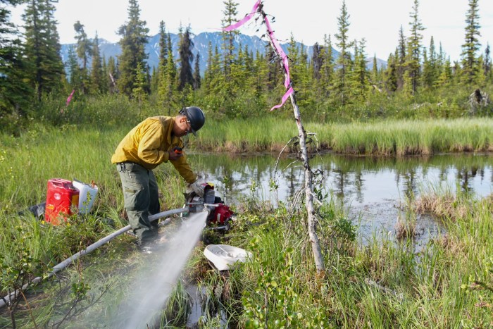 A firefighter discharges water from a pump on the NelchIna Glacier Fire.