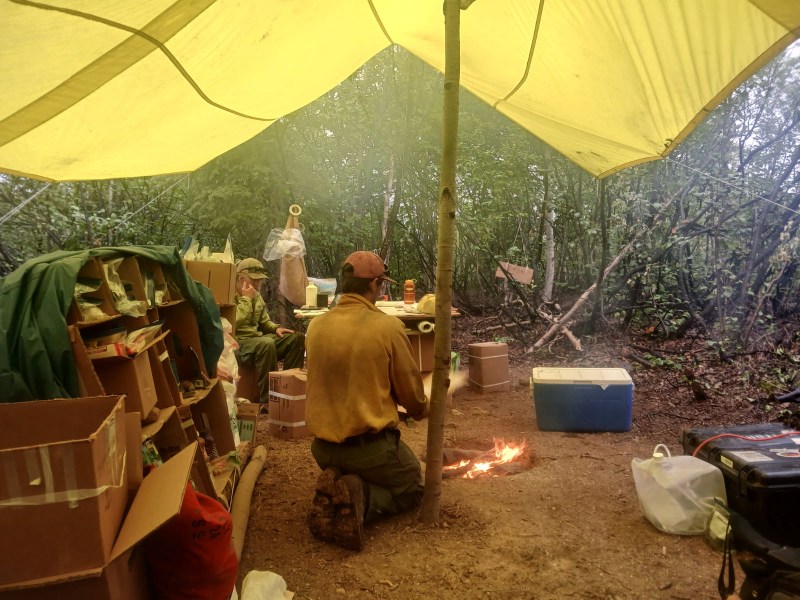 A firefighter huddles beneath a yellow tarp surrounded by hastily organized supplies.