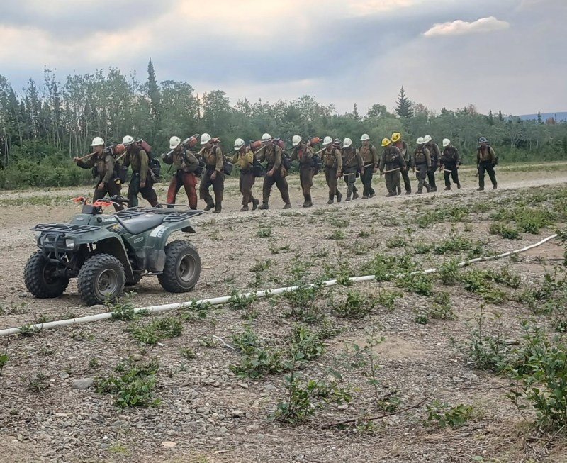 Firefighters in uniform marching beside a hoselay with an ATV in the foreground