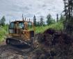 A bulldozer pushes a pile of dirt and woody debris.