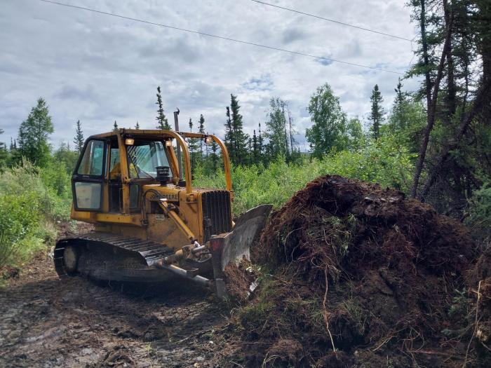 A bulldozer pushes a pile of dirt and woody debris.