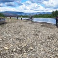 Several people are standing next to two boats on a gravel riverbed.