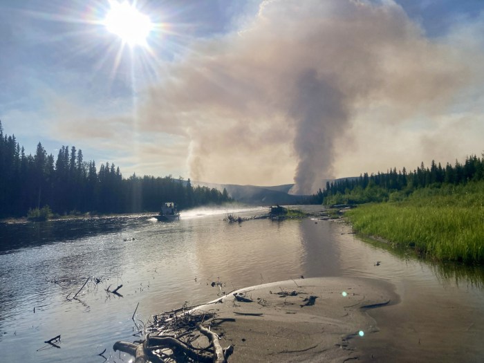 A large smoke plume is visible at the far end of a river.