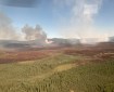 Aerial view of smoke rising from the ground near a burn scar in a forested area