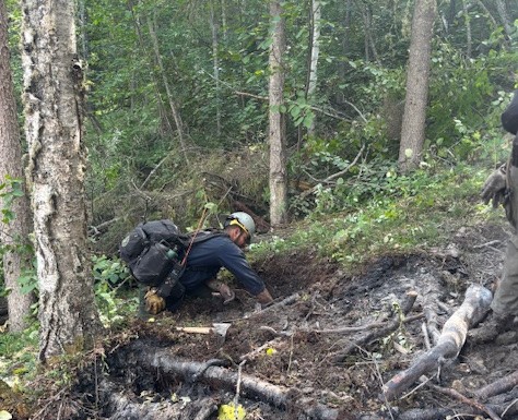 A man wearing a backpack is on his hands and knees while digging in the dirt.