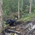 A man wearing a backpack is on his hands and knees while digging in the dirt.