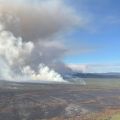 A large column of smoke drifts up from a burned area as seen from an aircraft.
