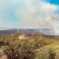 A firefighter stands on a mountain top looking down into wildfire smoke below him