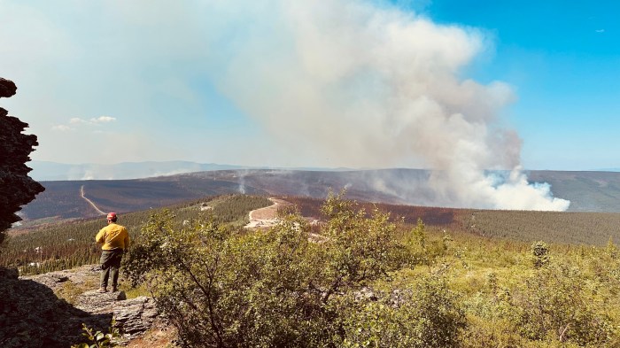 A firefighter stands on a mountain top looking down into wildfire smoke below him