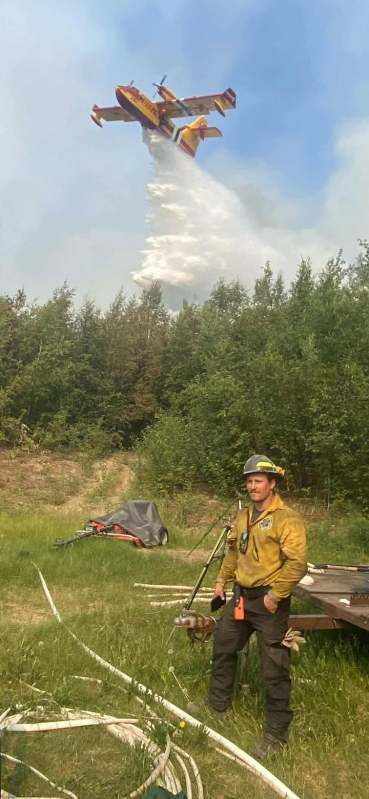 An air scooper aircraft drops a huge load of water on a fire as a fire fighter watches