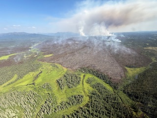 The burn scar from a fire continues to grow as smoke billows in the distance as the fire still burns.