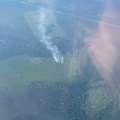 Photo from an airplane showing small parachutes of smokejumpers coming in over wildfire smoke in green vegetation.