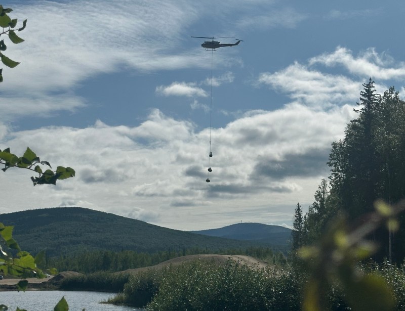 landscape view of helicopter hovering over helibase with supplies and equipment hanging from long line under helicopter