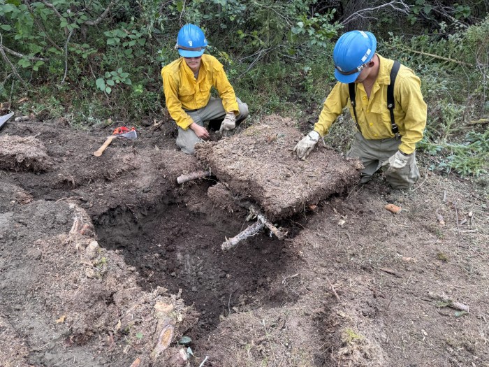 Two firefighters put kneeling beside a tundra box dug in the ground.