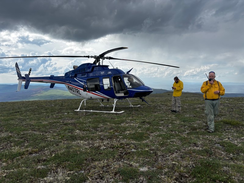 Helicopter on ground with two firefighters on the radio. 