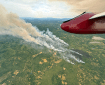 Smoke billowing up from a burned patch of green tundra. A red part of an aircraft wing is in the corner.