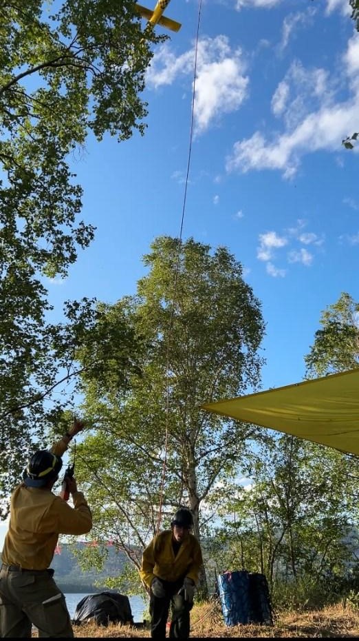 Image of firefighters hoisting equipment from a line connected to a helicopter.