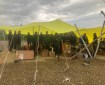 A group of 17 firefighters stand underneath a yellow tarp. The tarp is supported by wood posts and tied to the ground. The tarp covers most of the camp supplies for the firefighters.