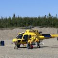 Firefighters in yellow shirts and hardhats load gear into a yellow helicopter.