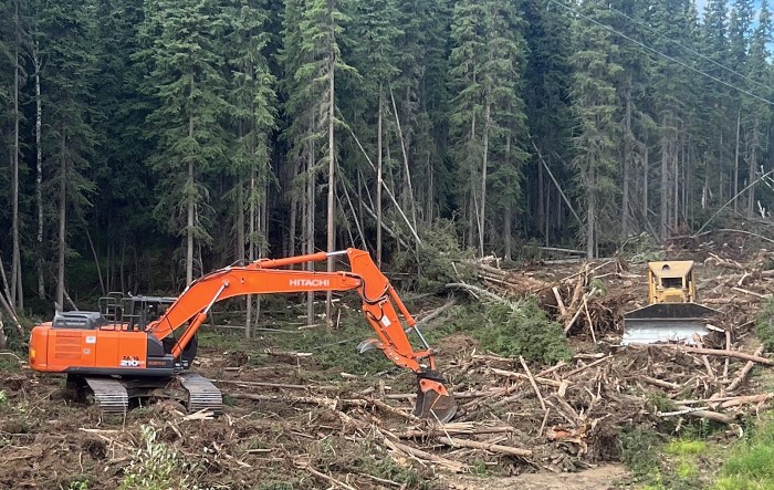 Heavy equipment covers a fireline with vegetative material in a forested area.