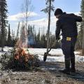 Person tends to small woody debris burn on gravel with an Alaska Burn Permit in their back pocket.