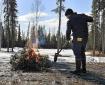 Person tends to small woody debris burn on gravel with an Alaska Burn Permit in their back pocket.