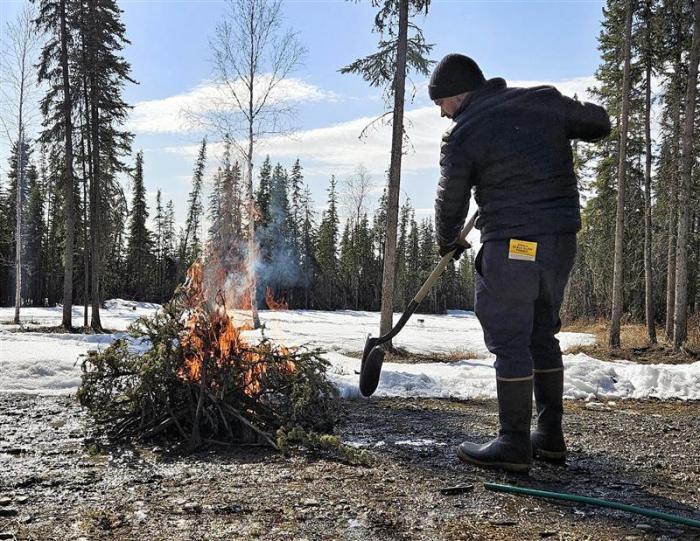 Person tends to small woody debris burn on gravel with an Alaska Burn Permit in their back pocket.