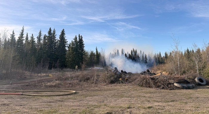 Smoke rises from a burning garbage pit in a forested area.