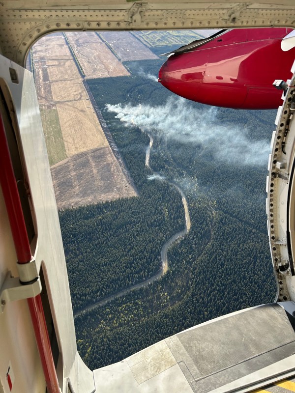 This aerial photo is looking through an aircraft's open door to a wildland fire burning below.
