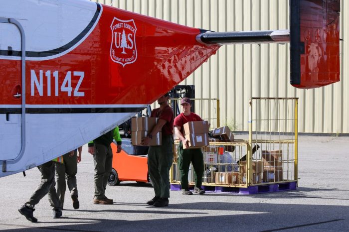 Firefighters load cardboard boxes of supplies into the back of an airplane.