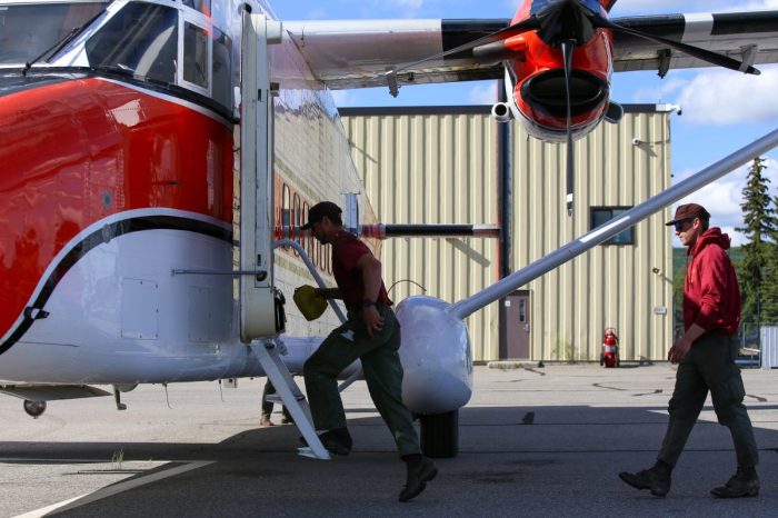 Two firefighters board an airplane.