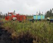 Orange Nodwell with attached trailer carrying a water tank is making its way through dense brush and Black Spruce. The black of the fire is seen in the front left corner of the photo.