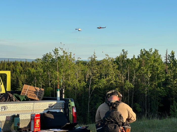 Photo of two helicopters with buckets attached with long lines.